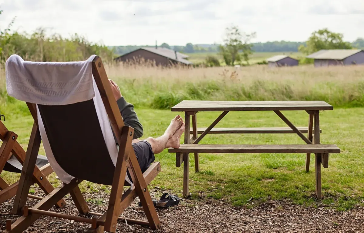 Deckchair and picnic bench outside a canvas hideaway at College Farm Beccles, with the other lodges across the field